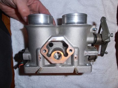 1990 Ford Bronco - A person holds a dual throttle body assembly, showing its metallic construction and mechanical components.