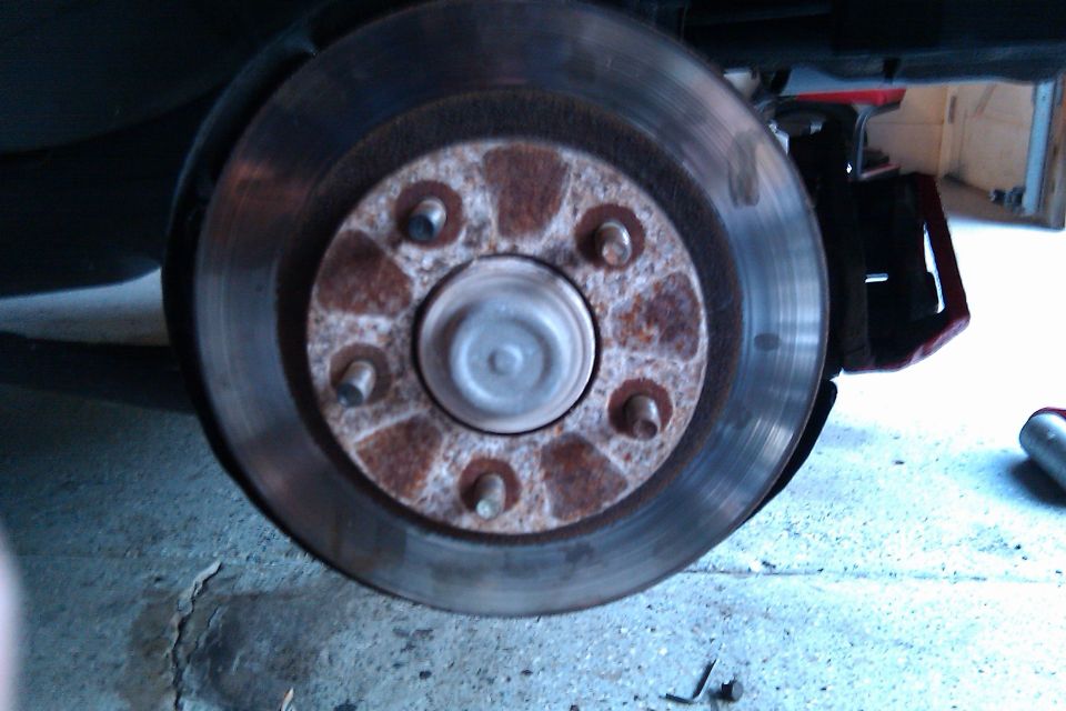 Rusty brake hub and rotor with five studs, wheel removed, car jacked up in garage