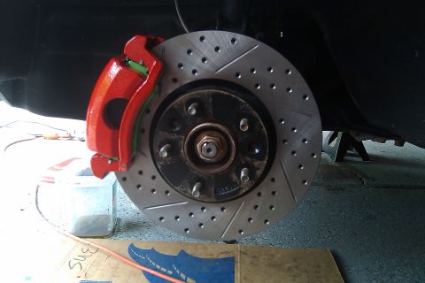 1996 Ford Probe - Close-up of a red brake caliper and a drilled rotor, with a vehicle supported by a jack stand in the background.