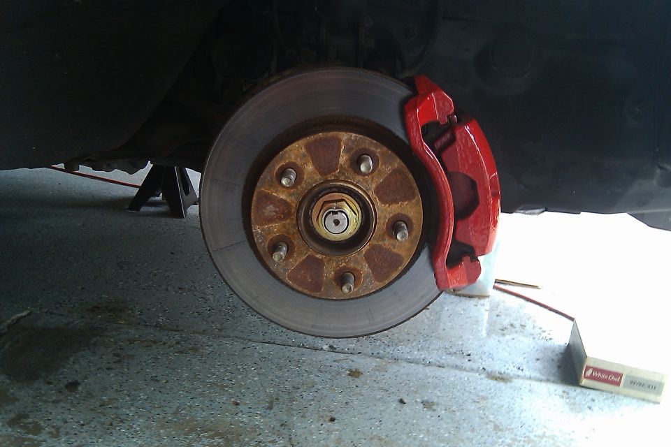 Car brake rotor with red caliper, supported by jack stands