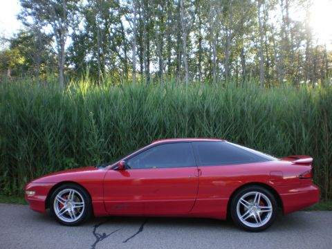 1996 Ford Probe - A red 1996 Ford Probe is parked on the side of the road with tall grass and trees in the background.