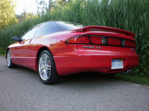 1996 Ford Probe - Rear-left view of a red 1996 Ford Probe coupe parked on an asphalt road with greenery in the background.