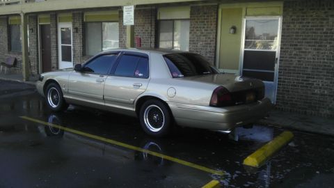 2000 Mercury Grand Marquis - A gold sedan with black rims is parked outside a brick building on a wet day.