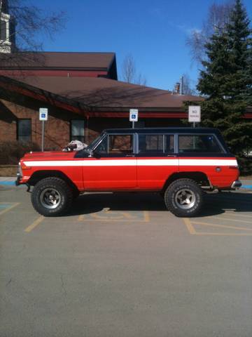 1990 Chevrolet Suburban - This red and black SUV with a white stripe is parked in a lot under a blue sky.