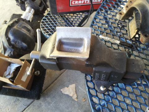 1978 Ford Bronco - A bench vise is holding a metal part with a stamped number. Other tools and parts are visible in the background.