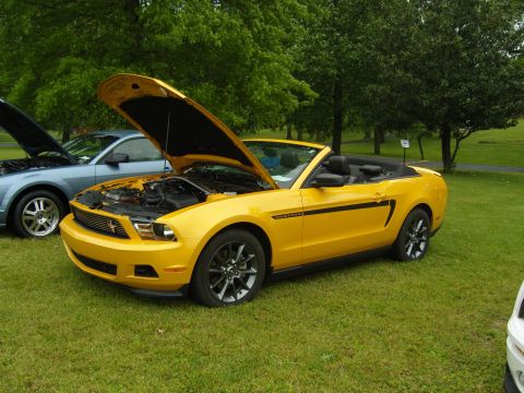 2007 Ford Mustang - A yellow convertible Mustang with its hood open is parked on a grassy field next to another car.