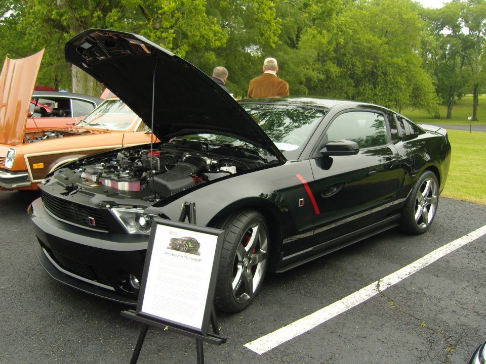 Black 2012 Ford Mustang GT with hood open, showing engine and a display sign