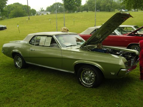 2007 Ford Mustang - A green 1969 convertible is displayed with its hood open, parked on a grassy field next to a red car.