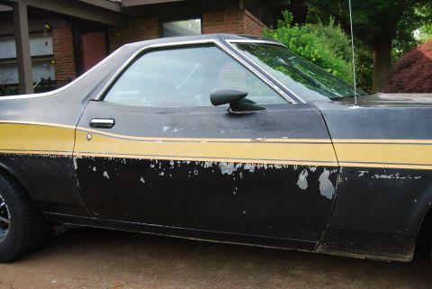 1975 Ford Ranchero - The side of a black 1975 Ford Ranchero shows significant paint damage along the yellow stripe.
