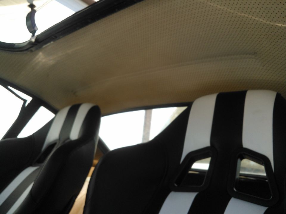 Car interior showing beige perforated headliner and black bucket seats with white stripes