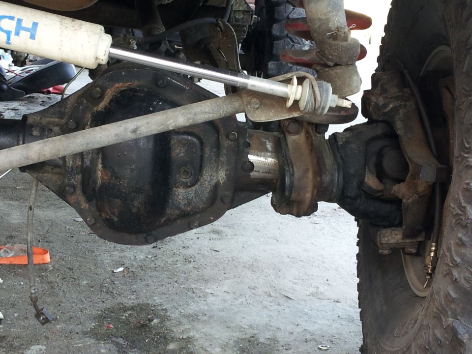 Close-up of a vehicle's front axle, steering linkage, and shock absorber
