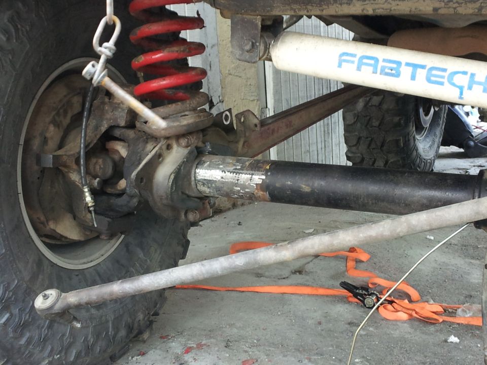 Close-up of a vehicle's front axle, red coil spring, and Fabtech shock absorber