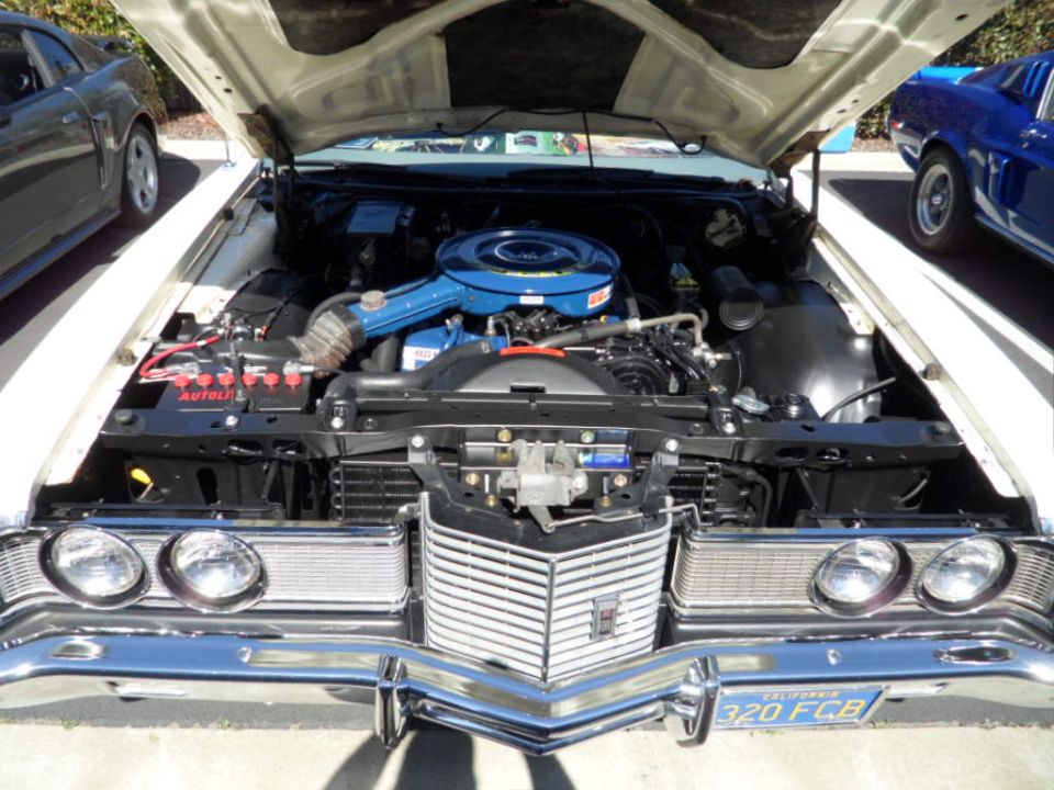White classic car engine bay with blue air cleaner and chrome grille. Two other cars visible