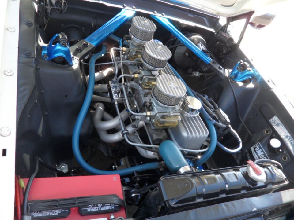 V8 engine with triple carburetors, blue strut tower brace, and red battery