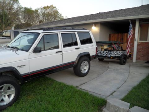 1994 Jeep Cherokee - A white Jeep Cherokee is parked on a driveway, hitched to a trailer loaded with items.