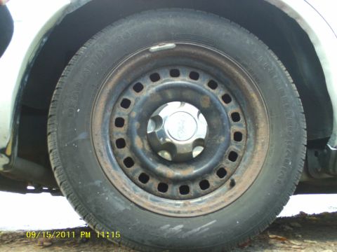 1998 Ford Crown Victoria - A close-up view of a rusty steel wheel with a chrome hubcap.