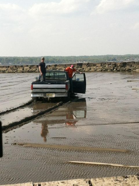 1990 Ford Bronco - Two people stand by a truck that is stuck in the mud, leaving tire tracks behind.