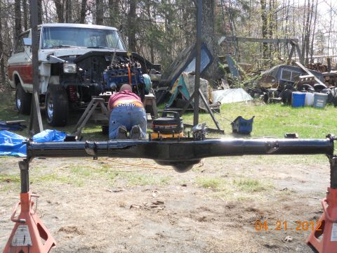 1978 Ford Bronco - A mechanic works on a 1978 Ford Bronco with its engine out, supported by stands.
