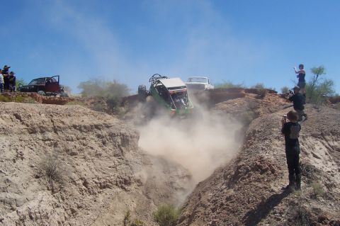 1981 Ford F-150 - Spectators observe as an off-road buggy tumbles down a dusty ravine, with a white pickup truck parked nearby.