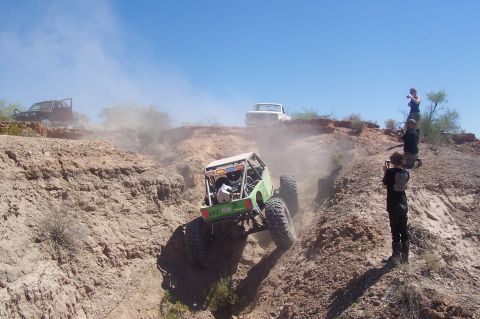 1981 Ford F-150 - Off-road vehicles navigate a steep, dusty incline under a clear blue sky, with spectators observing the action.