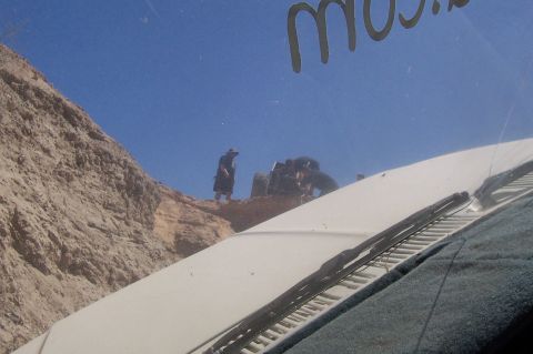1981 Ford F-150 - People and off-road vehicles are on a rocky incline under a bright blue sky, viewed from inside a vehicle.
