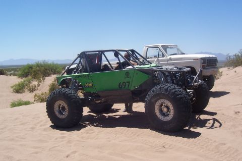 1981 Ford F-150 - A white Ford pickup truck is visible behind a custom green off-road buggy in a sandy desert landscape.