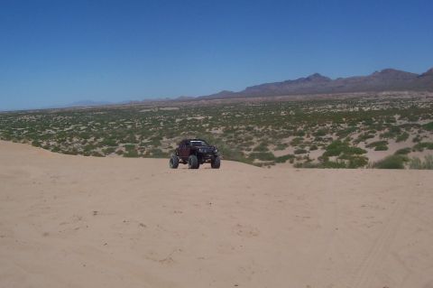 1981 Ford F-150 - A modified off-road truck navigates a sandy terrain with mountains in the background.