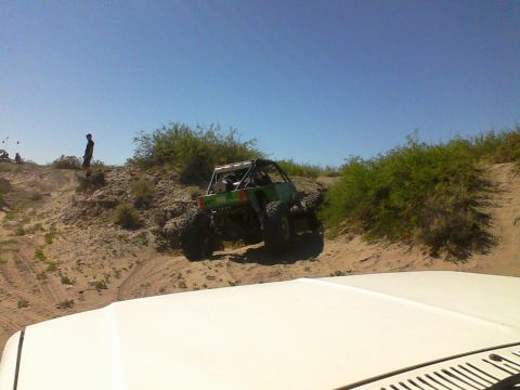 1981 Ford F-150 - A custom green off-road buggy navigates a steep, sandy incline under a clear blue sky, with another vehicle's hood in the foreground.