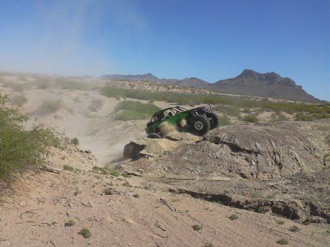 1981 Ford F-150 - A green off-road buggy navigates a dusty, rocky landscape under a clear blue sky.