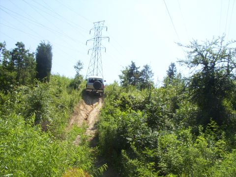 1995 Ford Bronco - SUV navigates a steep dirt path under a tall power line tower.