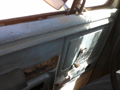 1981 Ford F-150 - Close-up of a vehicle's interior door panel, showing the window crank and a textured speaker grille.