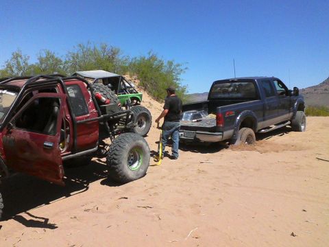 1981 Ford F-150 - A blue pickup truck is stuck in the sand, with a red off-road vehicle and a green buggy nearby.