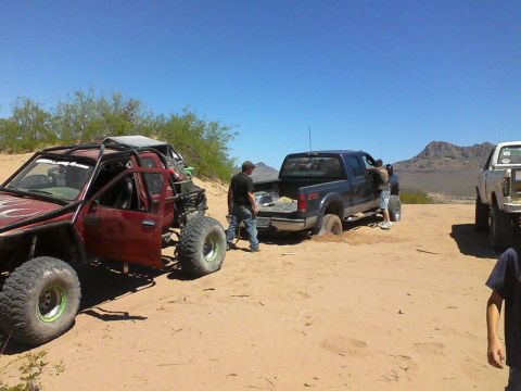 1981 Ford F-150 - Several off-road vehicles are in a sandy, desert environment with people around one of the trucks.