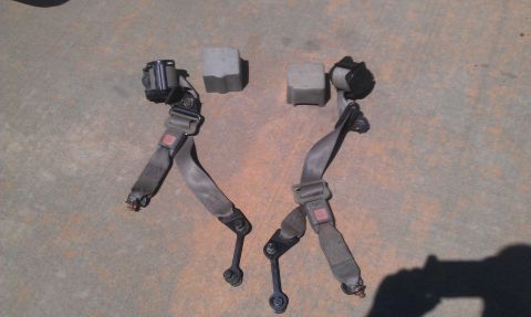 1991 Ford Festiva - A pair of used seat belts are laid out on the ground next to two small plastic blocks.
