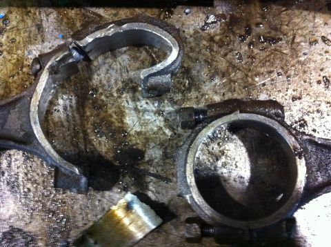 1990 Ford Bronco - Damaged engine connecting rods lie on a stained surface, indicating a severe mechanical failure.
