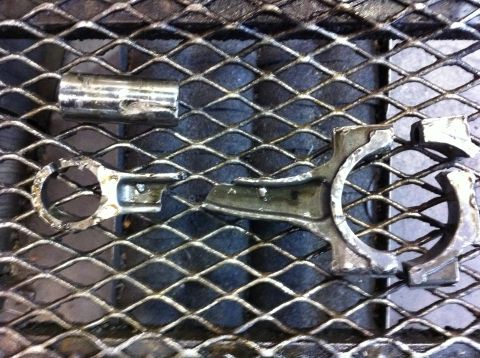 1990 Ford Bronco - Engine connecting rod and cap broken apart, resting on a metal grate.