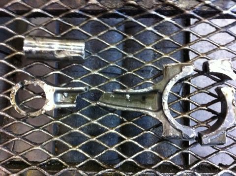 1990 Ford Bronco - This is a broken engine connecting rod and its cap, resting on a metal grate.