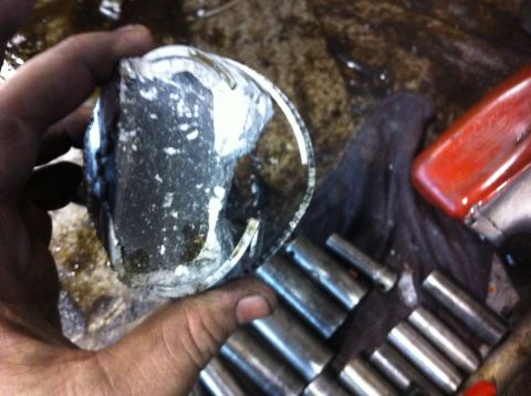 1990 Ford Bronco - Damaged engine piston held in hand, with tools nearby.