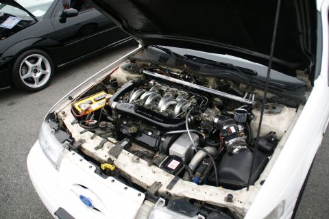 1993 Ford Taurus - The V6 engine of a white 1993 Ford Taurus is visible with the hood open, alongside another black car.