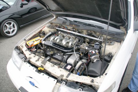 1993 Ford Taurus - The engine bay of a 1993 Ford Taurus, showing the V6 engine and other components. A black car is visible to the left.