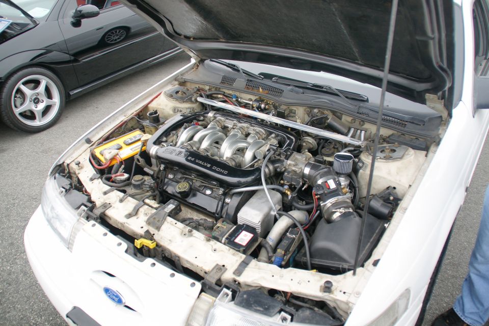 White 1993 Ford Taurus engine bay with a V6 engine. Another black car is parked next to it