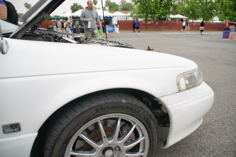 1993 Ford Taurus - A white sedan is parked outside with its hood open, showing the engine bay. People and tents are visible in the background.