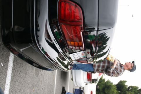 1993 Ford Taurus - A black car's rear bumper and taillight are visible, with a license plate attached. Another vehicle is partially seen in the background.