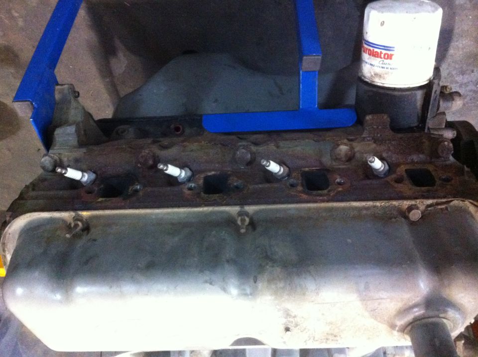 Engine block with spark plugs installed and an oil filter on top. Blue engine hoist component is visible