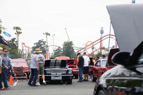 1993 Ford Taurus - A black 1967 Ford Mustang with racing stripes is displayed at an outdoor car show with roller coasters in the background.