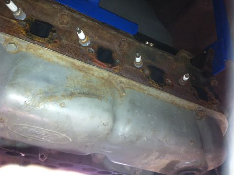 1990 Ford Bronco - Close-up view of a rusty engine component, possibly an oil pan, with spark plugs installed.