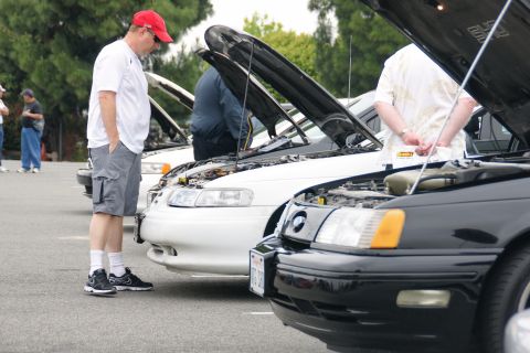 1993 Ford Taurus - Several cars, including a 1993 Ford Taurus, are parked with their hoods open at an outdoor gathering.