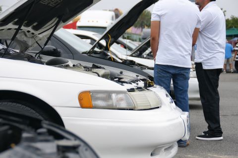 1993 Ford Taurus - Two men look at a white 1993 Ford Taurus with its hood open at an outdoor car event.