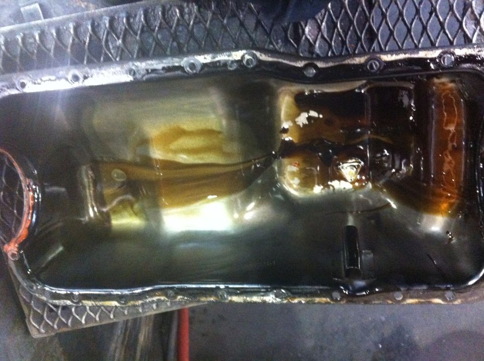 engine oil pan with dark oil and some lighter sludge inside