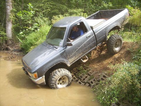 1995 Ford Bronco - Pickup truck navigates a muddy off-road trail with water obstacles.